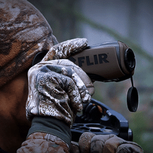 Man wearing camouflage looking through a Teledyne FLIR Scout III handheld thermal monocular.