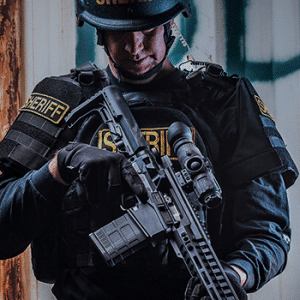 Police officer in SWAT gear holding a AR-15 rifle with a Trijicon IR-Patrol thermal monocular mounted to it.