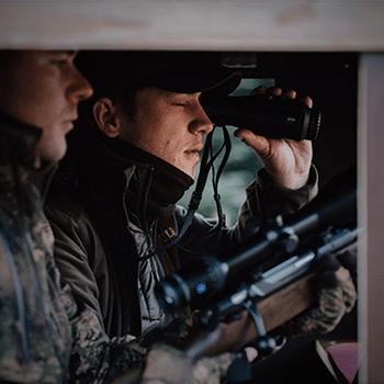 Photo of two hunters. One is looking through a Zeiss DTI 3/35 thermal imaging camera while the other is holding a bolt-action rifle waiting to take a shot.