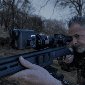 Man shown aiming a rifle with a Proton FXQ30 thermal imaging front attachment mounted to it.