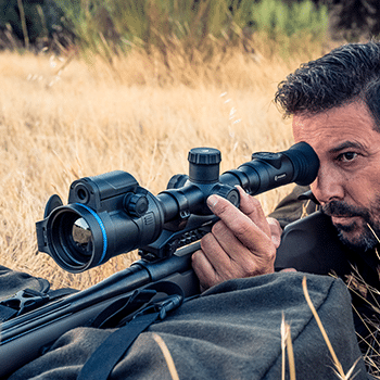 Pulsar Thermion Duo thermal riflescope shown attached to a bolt-action rifle with a man looking through the lens.